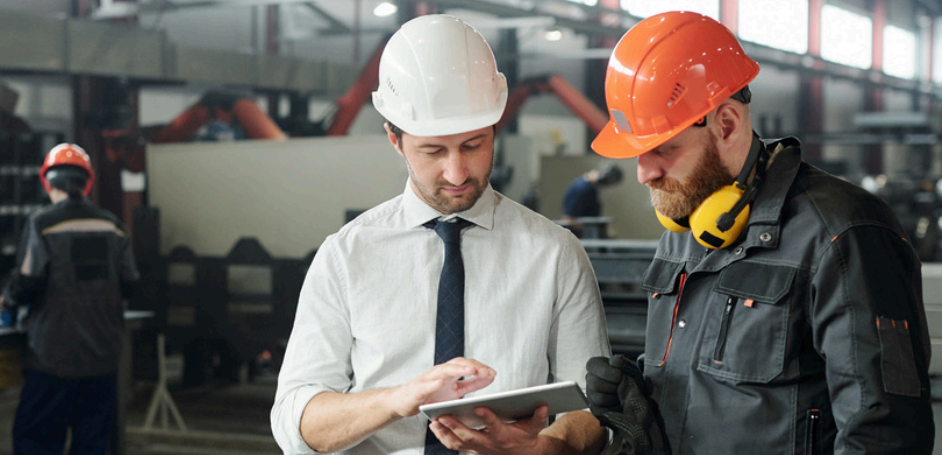 Two men in hardhats working on the floor of a manufacturing plant.